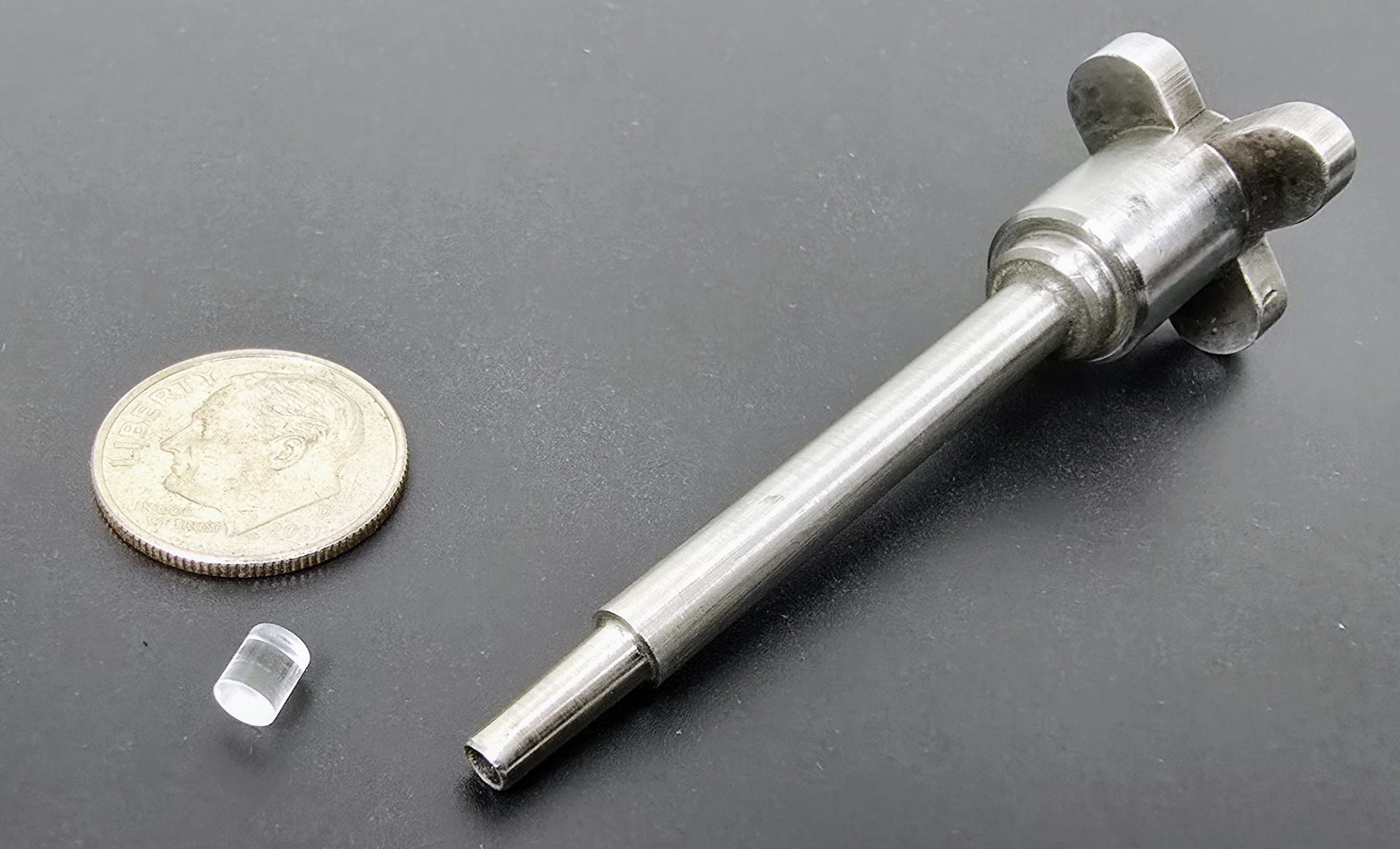 A plastic replica of the pellets formed by the system on W7-X, next to a dime, for size reference, and the cutter that extracts the pellet from the extrusion, as seen in the video.